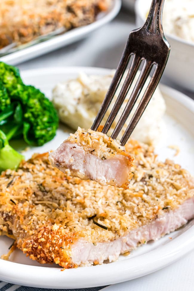 parmesan crusted pork chop on a dinner plate with a bite on a fork
