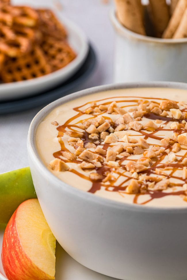 apple dip in a bowl with caramel and chopped peanuts on top