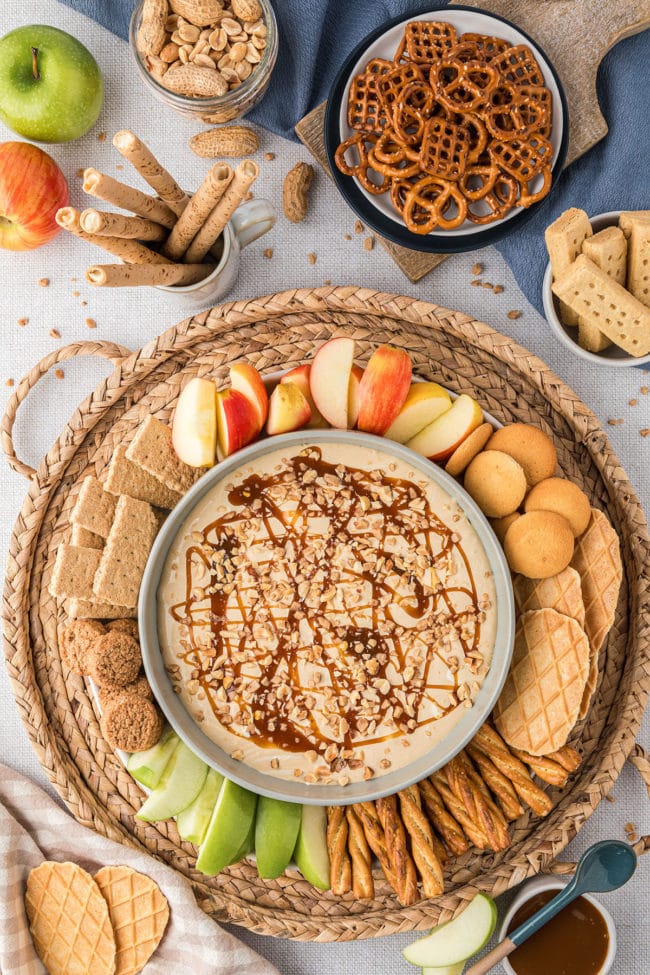 caramel apple dip on a tray with apple slices, cookies, pretzels and more