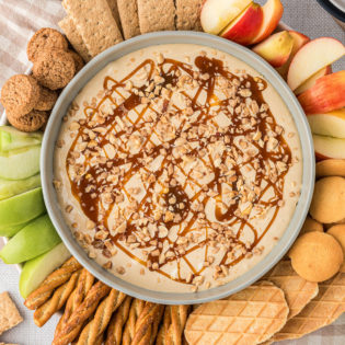 dessert dip in a bowl with apples, cookies and graham crackers all around it.