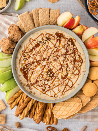 dessert dip in a bowl with apples, cookies and graham crackers all around it.