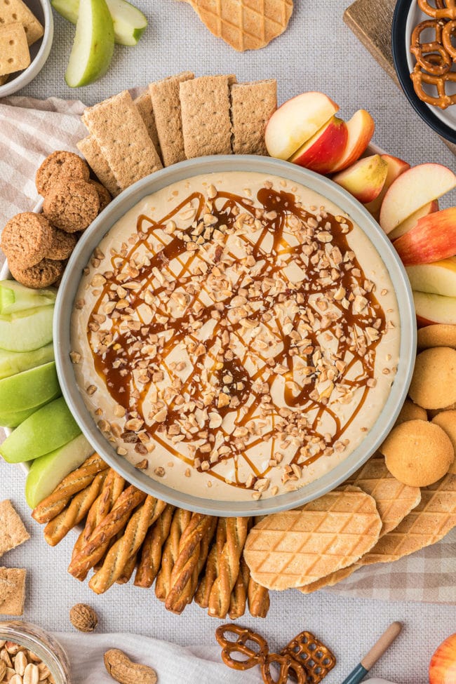 dessert dip in a bowl with apples, cookies and graham crackers all around it.