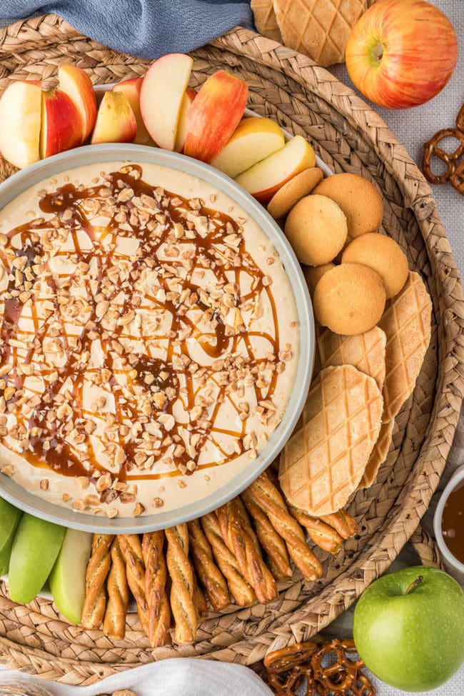 dessert dip in a bowl with apples, cookies, pretzels, and graham crackers all around it.