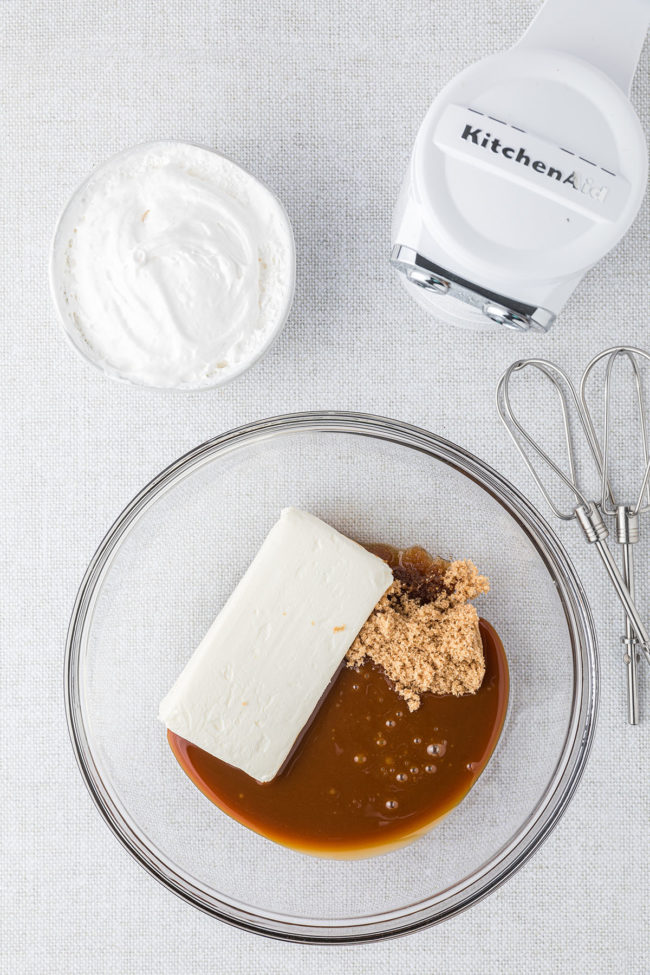 cream cheese, caramel topping and brown sugar in a glass mixing bowl with an electric beater
