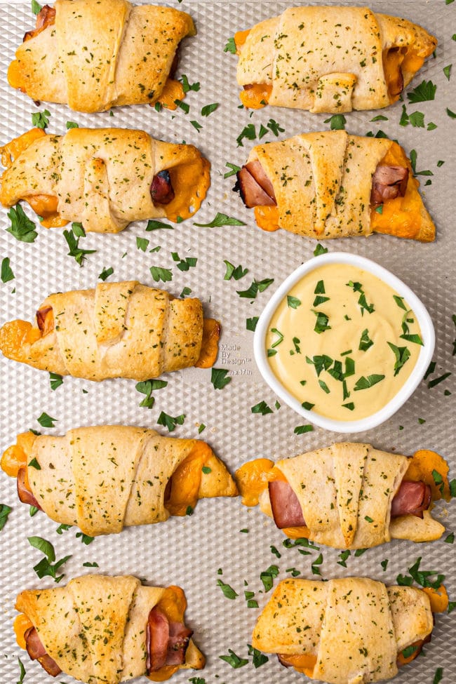 Ham and Cheese Roll-Up Sandwiches on a baking sheet with dipping sauce