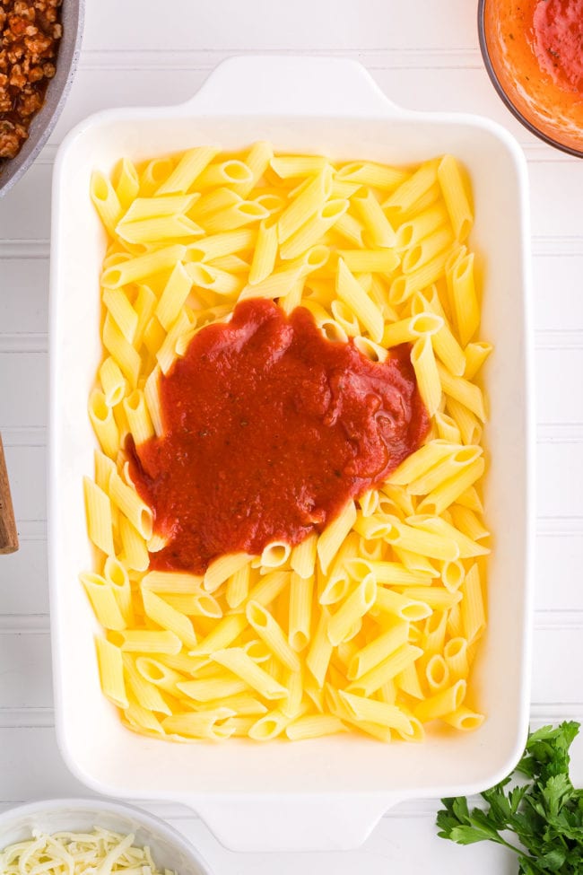 cooked penne pasta in a white baking dish with a little pasta sauce