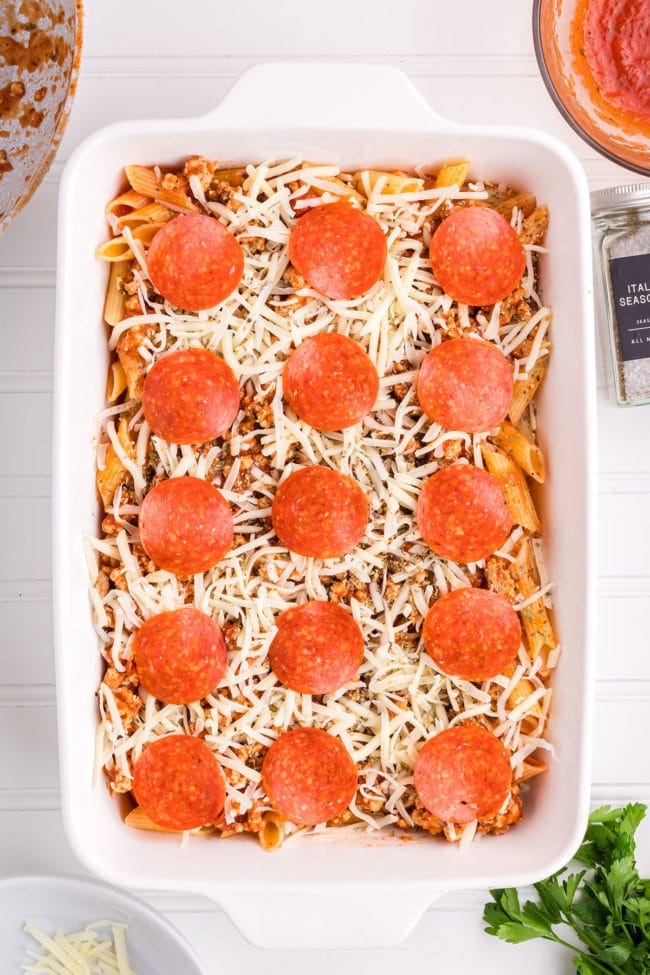a baking dish with cooked pasta, ground chicken in red sauce with shredded cheese and pepperoni