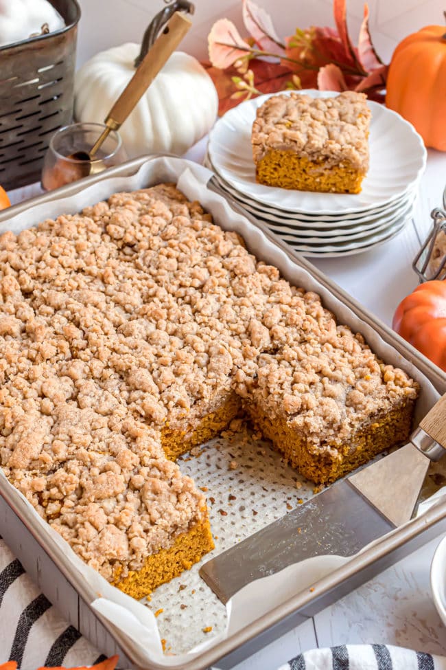 Baked pumpkin coffee cake with crumb topping in a cake pan with a few servings on plates