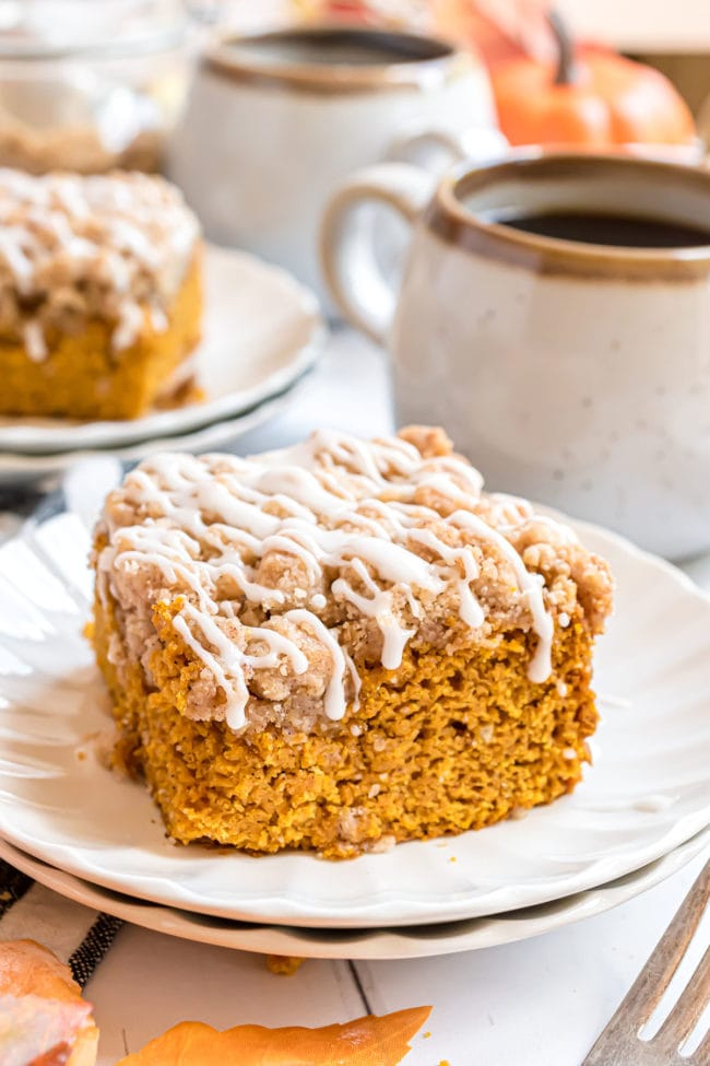 pumpkin coffee cake with vanilla glaze on a white plate with cup of coffee