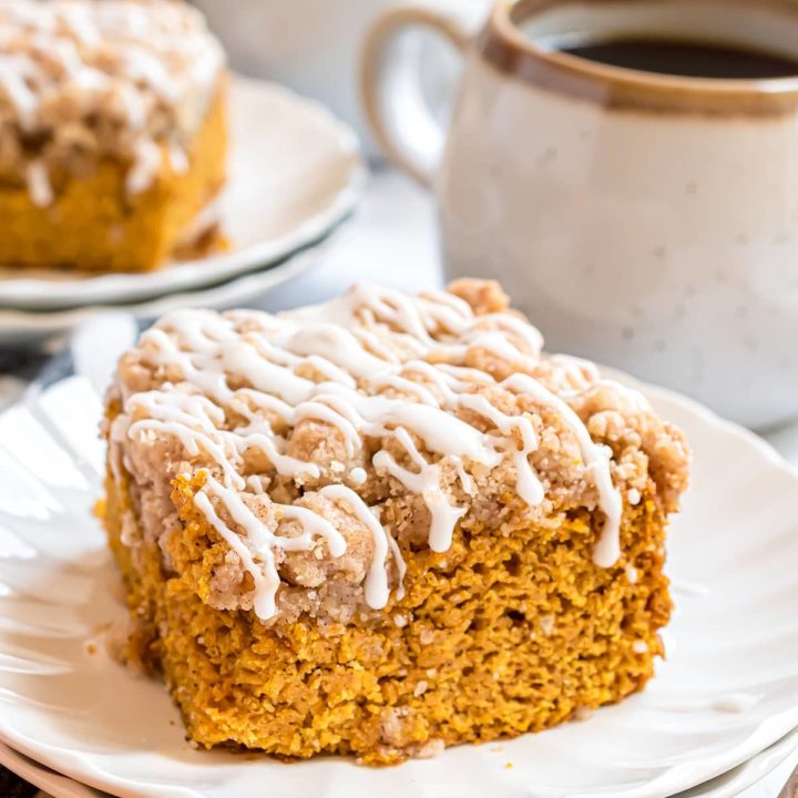 pumpkin coffee cake with vanilla glaze on a white plate with cup of coffee