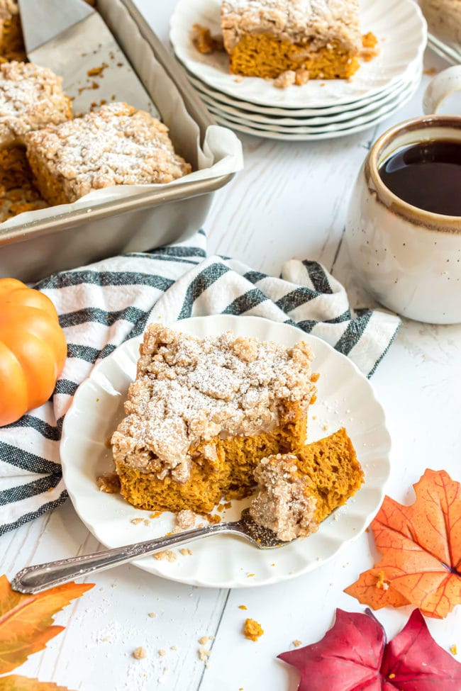 pumpkin cake on a dessert plate with a bite of cake on a fork. Cup of coffee and cake pan in background