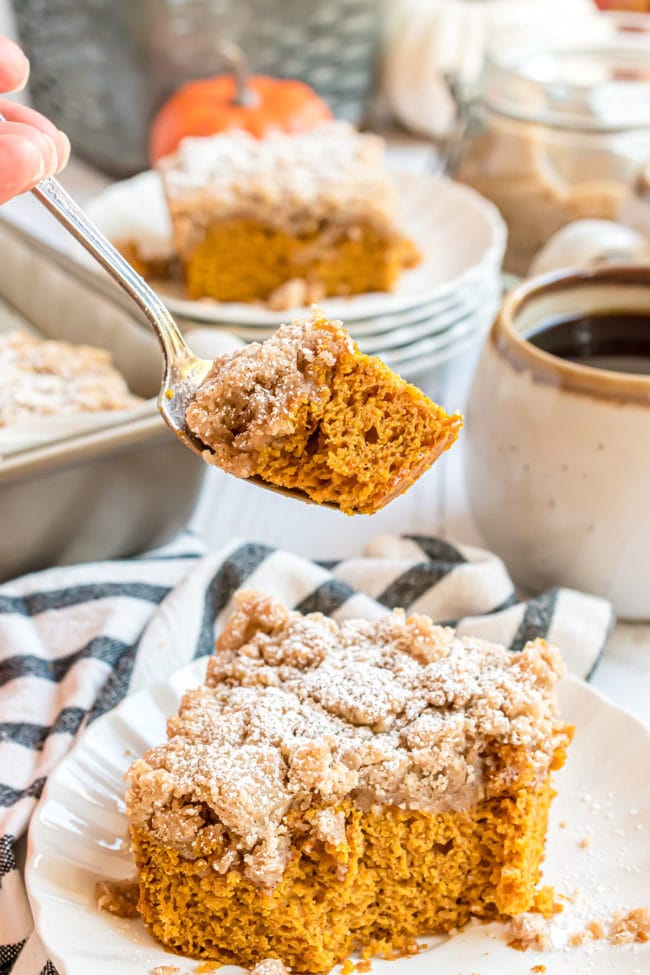 A bite of pumpkin crumb cake on a fork over a plated serving of the cake