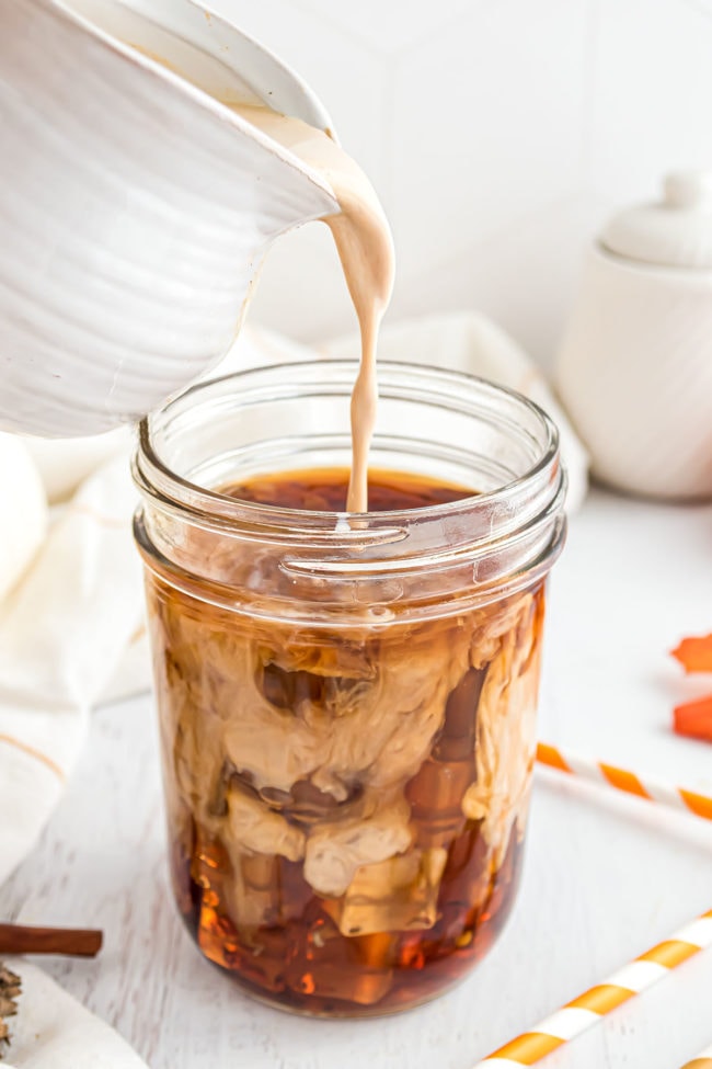 pouring Pumpkin Spice Coffee Creamer into a glass of cold-brewed coffee