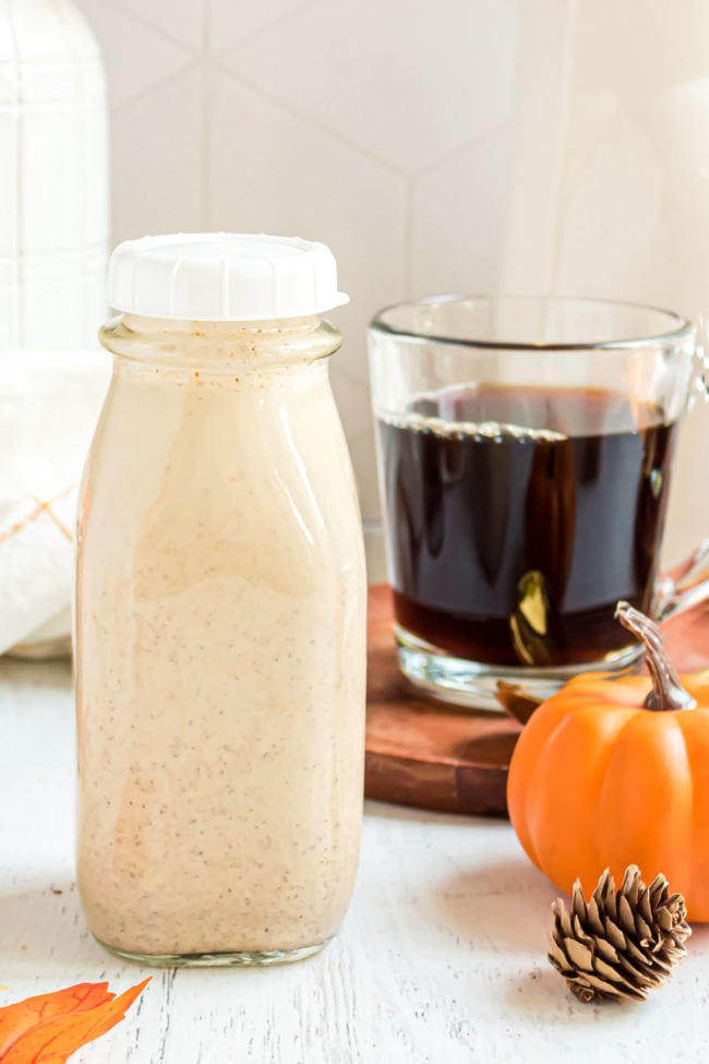 Pumpkin Spice Creamer in a bottle with a lid with a pumpkin and mug of coffee in the background