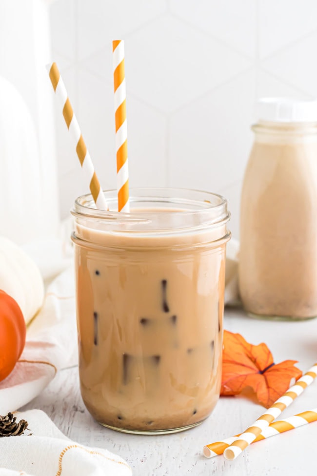 a glass of iced coffee with homemade pumpkin spice creamer and orange striped straws.