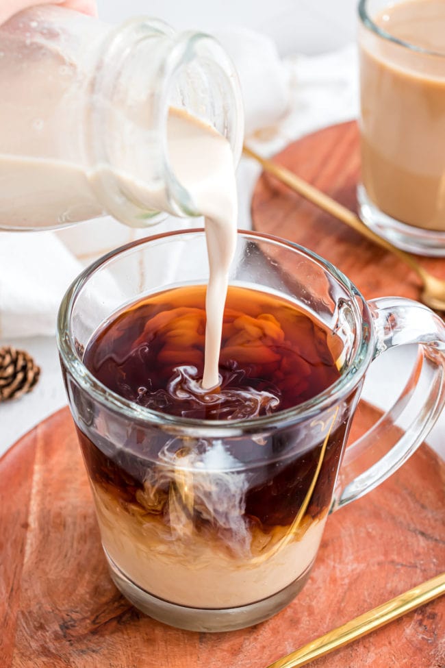 Pouring homemade creamer into a clear mug of coffee