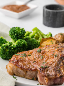 a plate with a glazed pork chop and steamed broccoli