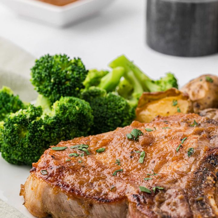 a plate with a glazed pork chop and steamed broccoli