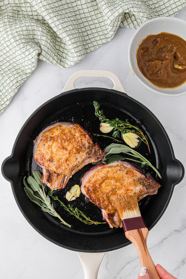 glazed pork chops in a cast iron skillet with fresh herbs
