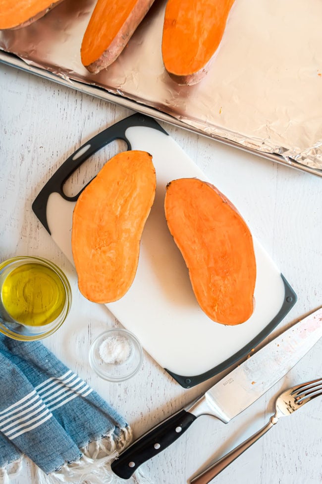 raw sweet potato cut in half lengthwise on a cutting board