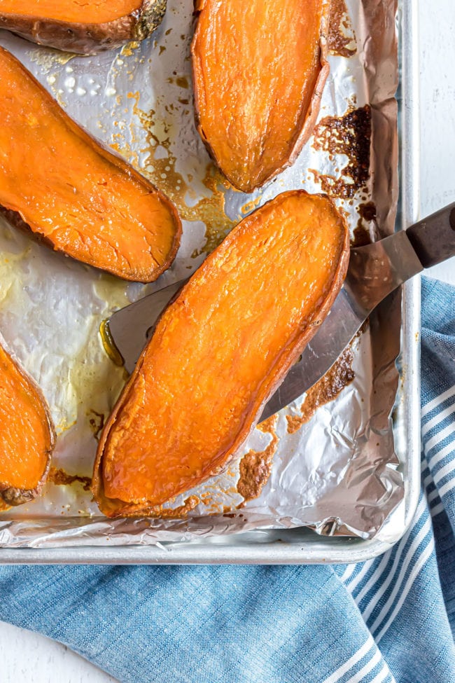 halved sweet potatoes on a baking sheet with a spatula