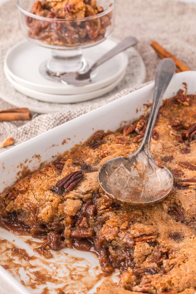 pecan pie cobbler in a baking dish with a serving spoon