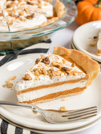 A pie with layers of pumpkin pie filling and whipped topping on a white plate with a fork