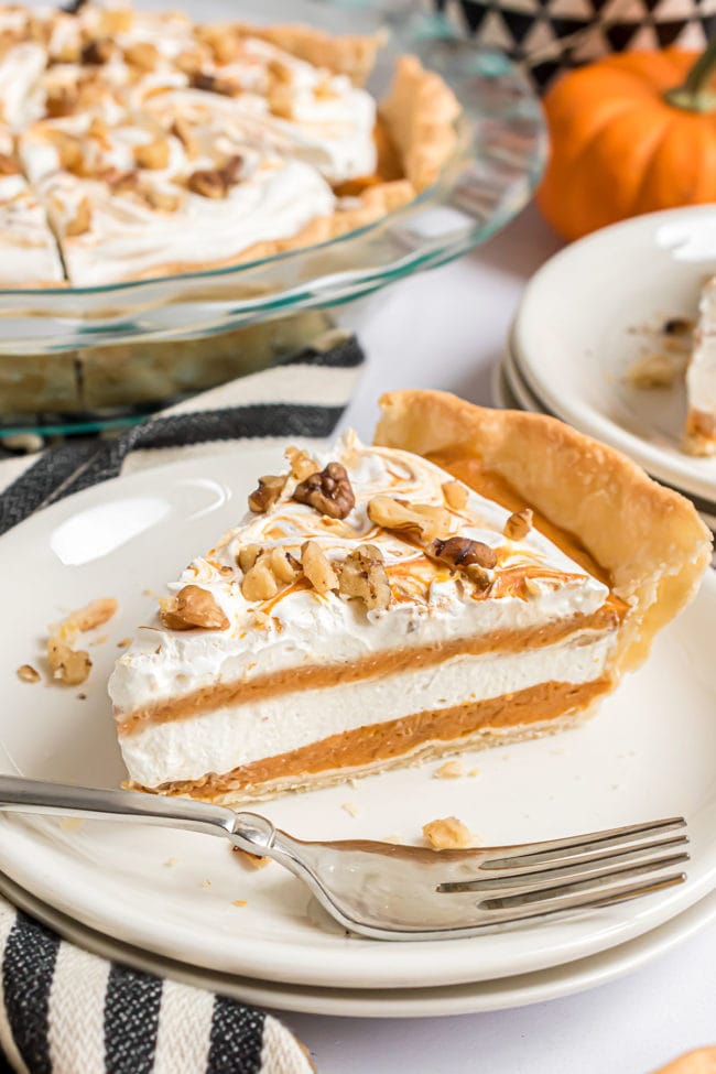 A pie with layers of pumpkin pie filling and whipped topping on a white plate with a fork