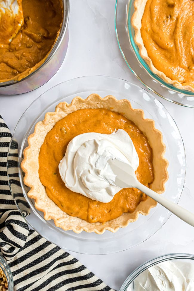 layering pie with cool whip over pumpkin pie filling in a baked pie shell