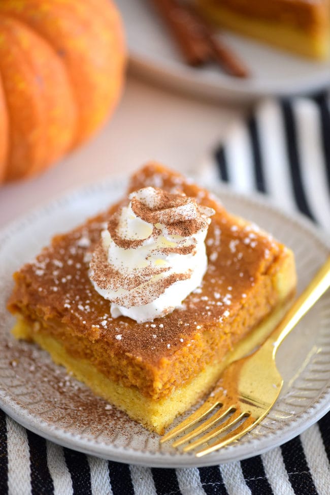 a serving of pumpkin ooey gooey cake with whipped cream on a plate with a gold fork