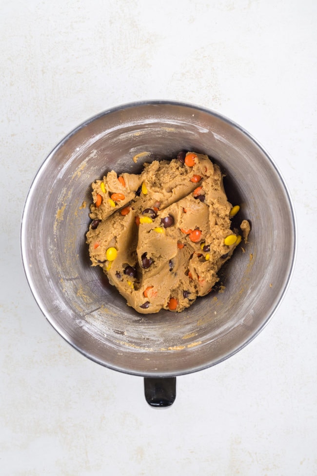 Reese's Pieces mixed into peanut butter cookie dough in a mixing bowl