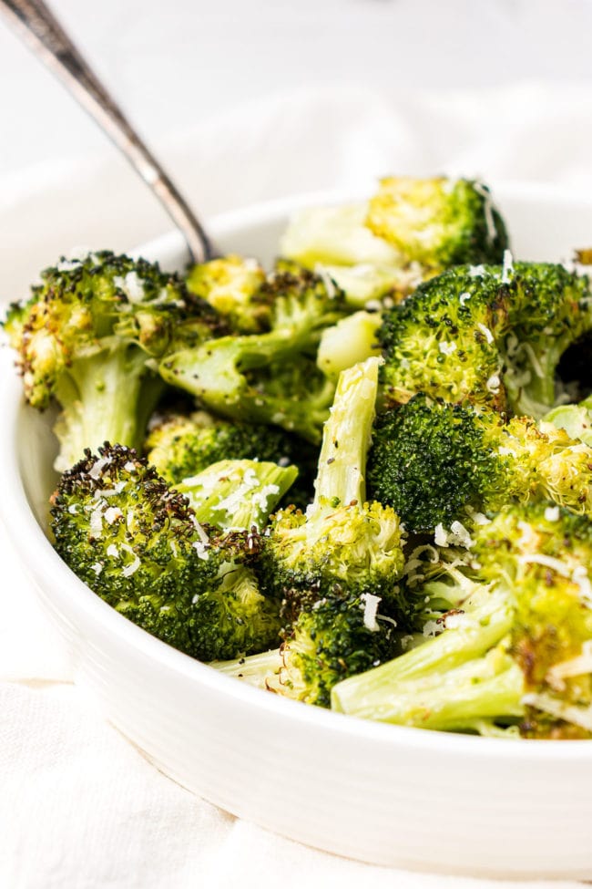 a bowl of parmesan oven roasted broccoli with a serving spoon