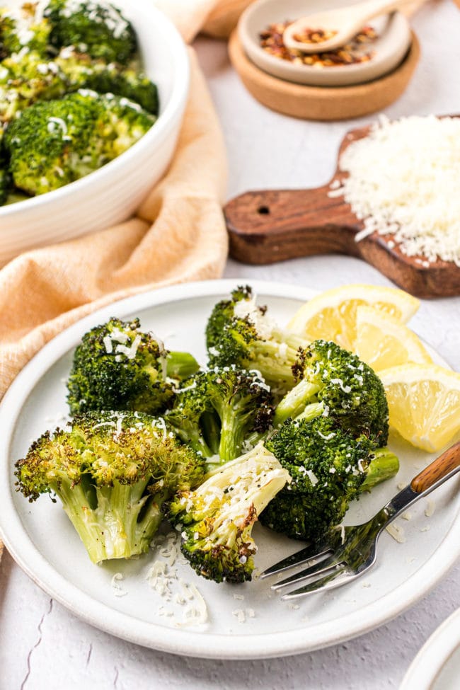 roasted broccoli on a plate with a fork and lemon wedges
