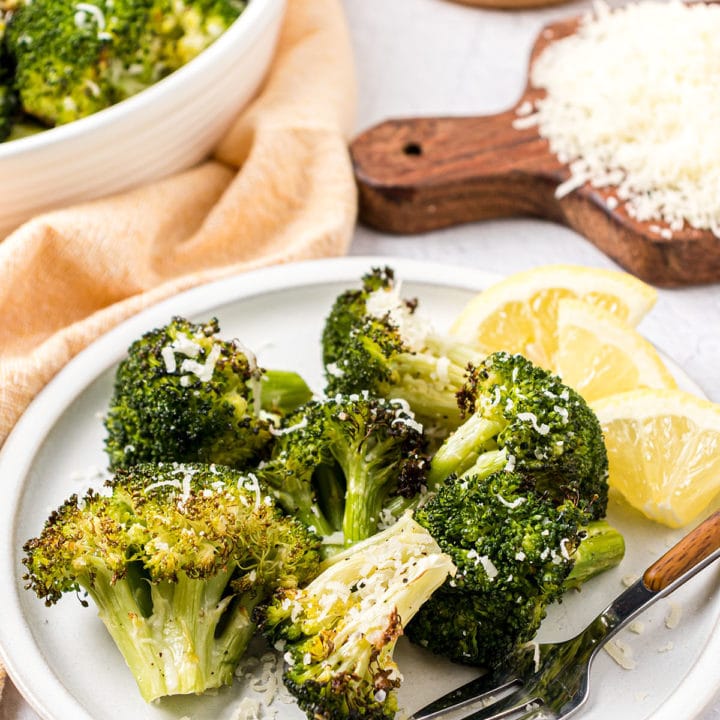 roasted broccoli on a plate with a fork and lemon wedges