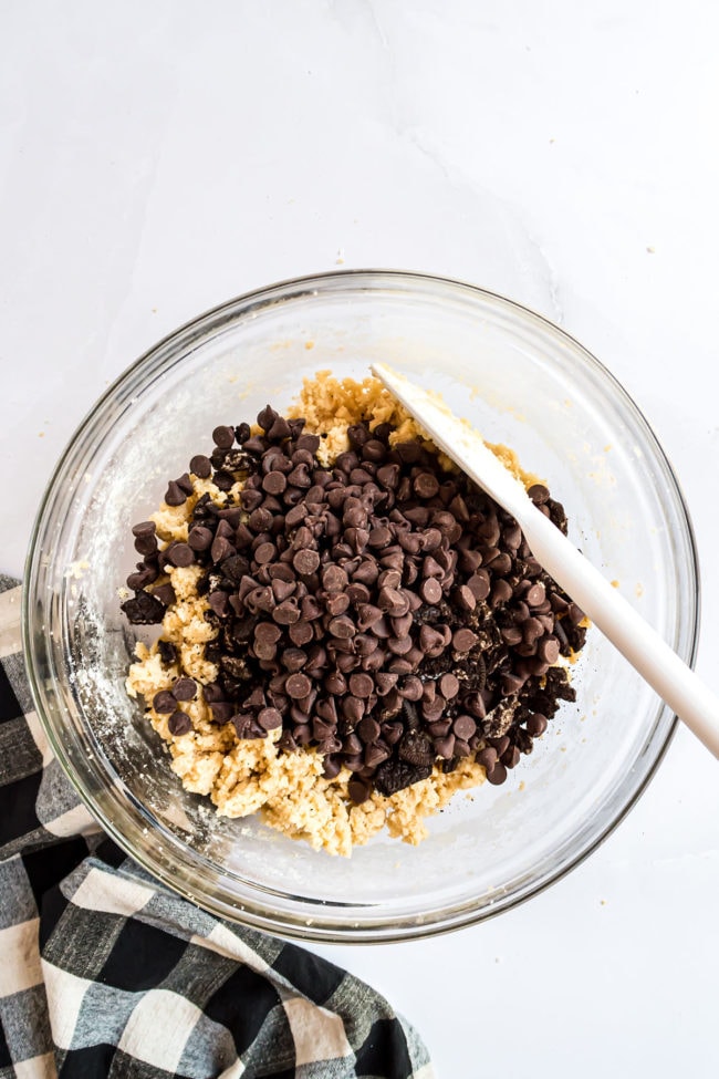 cookie dough in a clear mixing bowl with chocolate chips and crushed Oreos