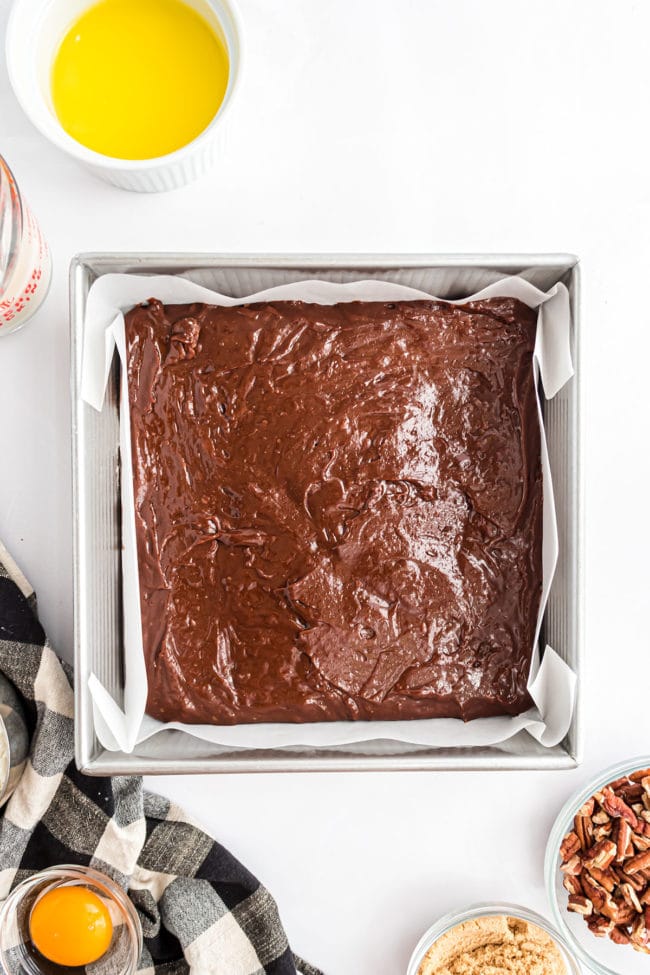 brownie batter in a square metal pan with parchment paper