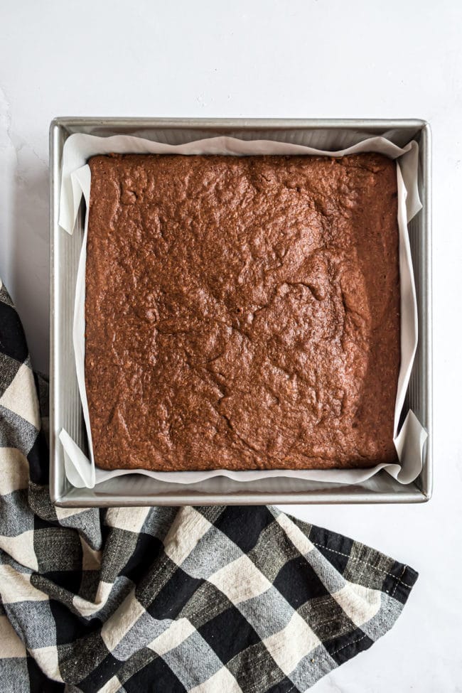 baked brownies in a square metal pan with a black checked towel on a counter
