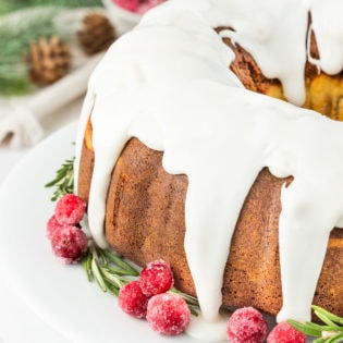 Gingerbread Bundt Cake with a glaze, garnished with sugared cranberries and rosemary sprigs