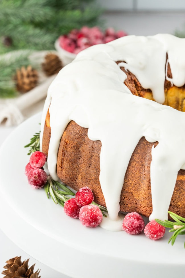 Gingerbread Bundt Cake with a glaze, garnished with sugared cranberries and rosemary sprigs