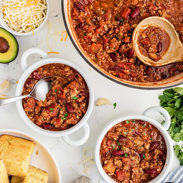 left over turkey chili in white bowls and large pot with cornbread on the side.