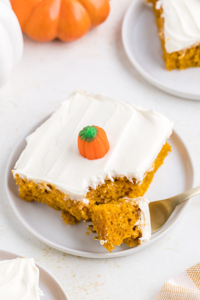 Fall cake with cream cheese frosting and a candy pumpkin on top. On a white plate with a fork