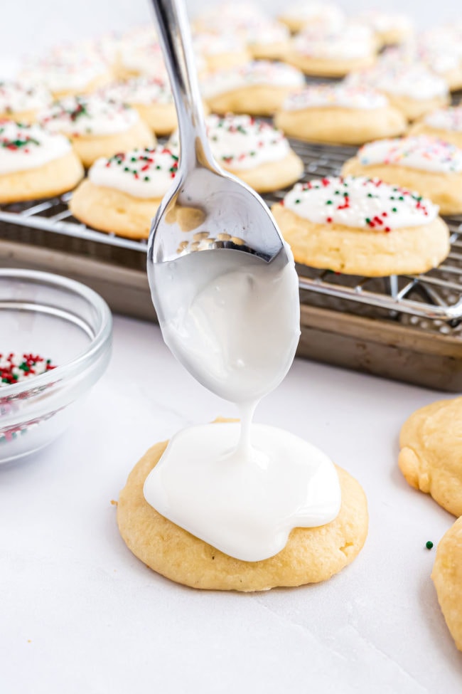 drizzling icing with a spoon on a ricotta cookie