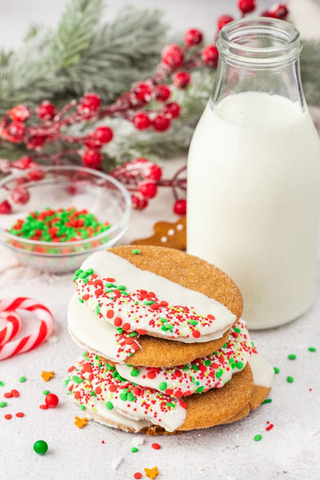 stack of chocolate dipped ginger cookies with holiday sprinkles and a bottle of milk
