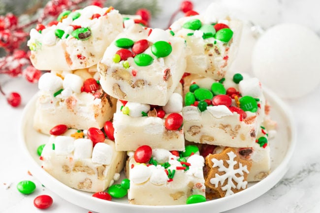 a stack of White Christmas Fudge with holiday candies on a white platter