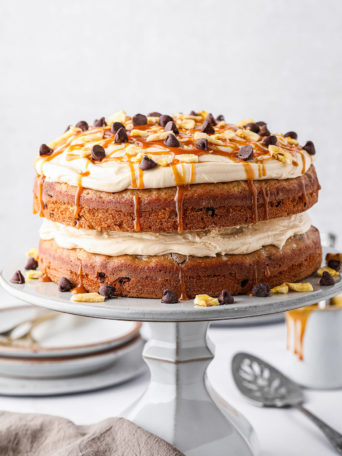 banana layer cake with salted caramel frosting topped with chocolate chips on a cake stand