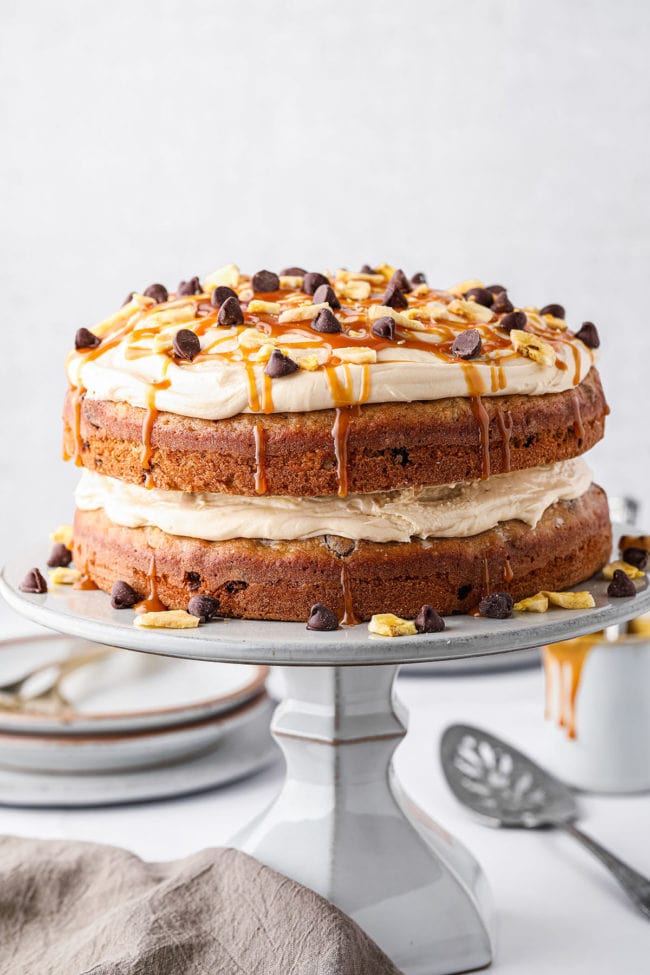 banana layer cake with salted caramel frosting topped with chocolate chips on a cake stand