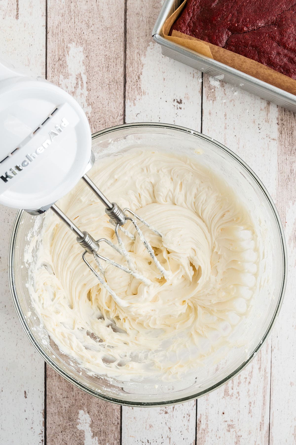 making cream cheese frosting with an electric hand mixer in a glass mixing bowl