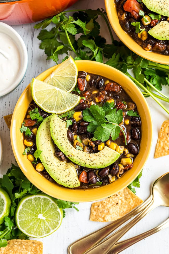 yellow bowl of black bean soup garnished with avocado and lime slices