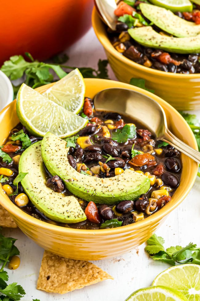 yellow bowl full of black bean soup garnished with avocado slices