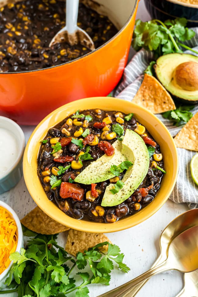 orange pot and yellow bowl full of black bean soup garnished with avocado slices